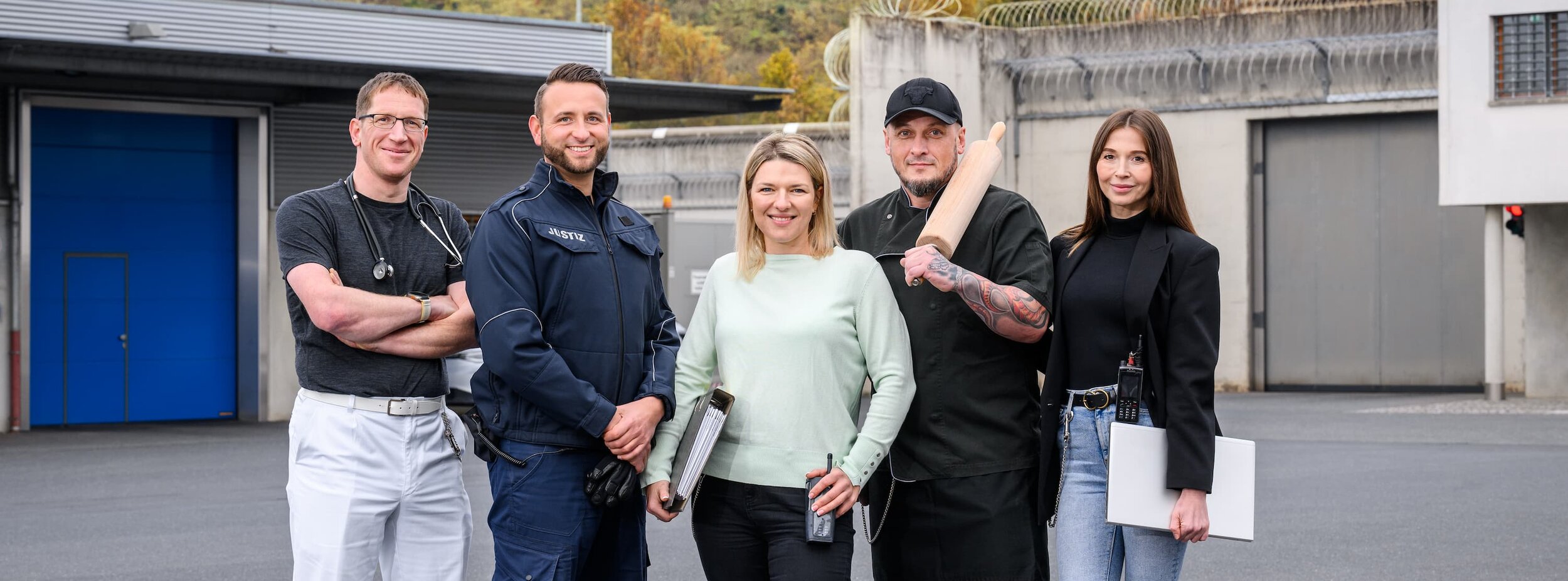 Fünf Mitarbeiter verschiedener Fachgebiete Justizvollzugs stehen auf dem Hof einer Justizvollzugsanstalt