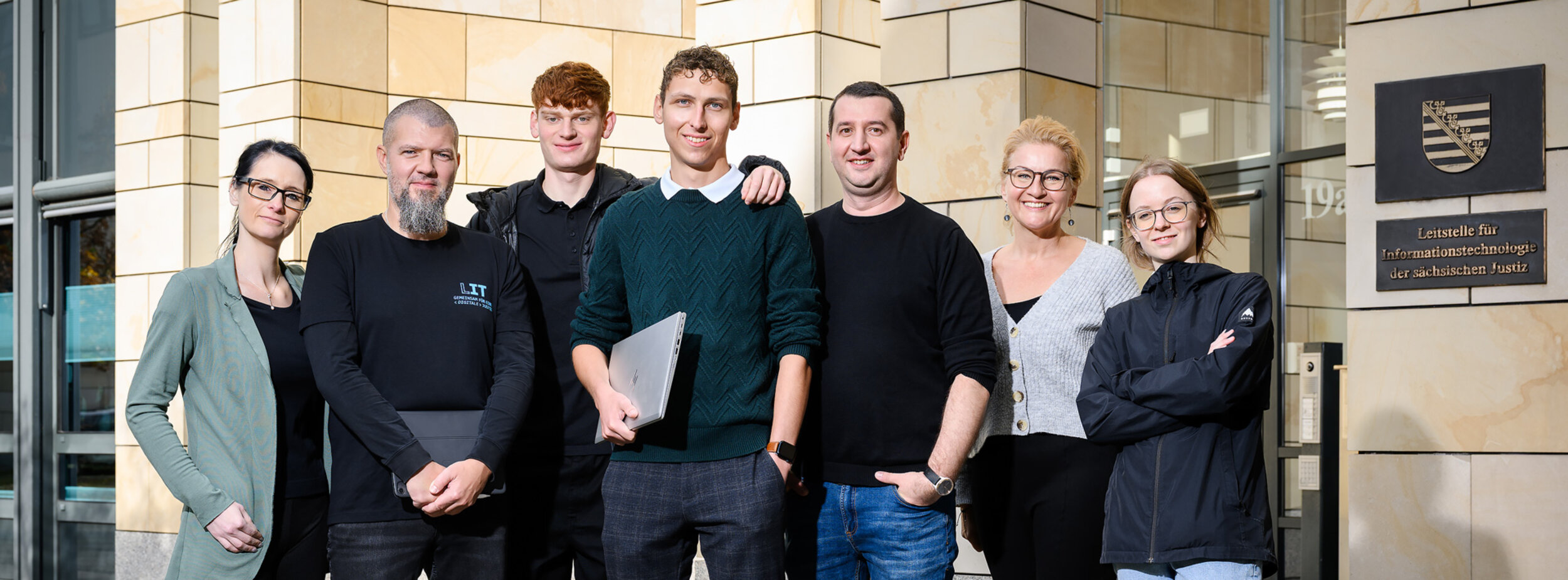 Eine Gruppe von Mitarbeitern verschiedener Fachgebiete der Leitstelle für IT stehen vor einem Gebäude